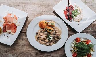 A stylish arrangement of various dishes on white plates. In the foreground, there is a creamy dish with poultry and mushrooms.