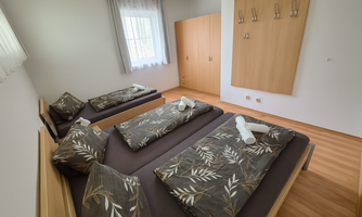 A bright room with two beds and a modern wooden wardrobe. The bedding has a trendy leaf pattern and there are some towels on the bedspreads.