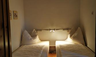 A cozy bedroom with two single beds and a round light. The walls are bright and the room feels inviting.