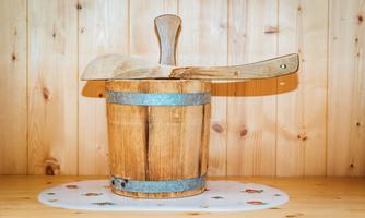 A wooden container with a wooden lid is standing on a table. The wall in the background is made of wooden panels.