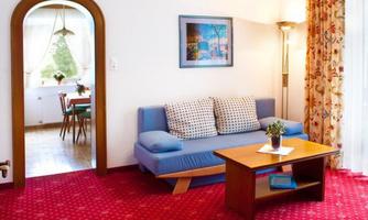 A cozy living room with a blue sofa and a wooden table. Through an arch, the dining area with a table and chairs is visible.