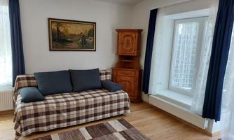 A cozy living room with a checked sofa and a wooden dresser. There are long, dark blue curtains at the windows and a rug on the floor.