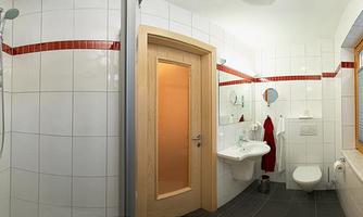 A modern bathroom with a shower, sink, and toilet. White tiles and red accents create a friendly atmosphere.