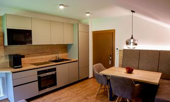 A modern kitchen unit with bright cabinets and modern appliances. Next to it is a dining area with a wooden table and comfortable chairs.