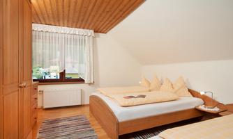 A cozy bedroom with two single beds and wooden furniture. Large windows let in plenty of light and offer a view outside.