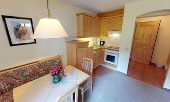 A cozy kitchen with wooden cabinets and a dining table. In the background, the door and a window can be seen.