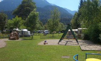 A beautiful playground in the midst of nature, surrounded by trees and mountains. In the background, campsites are visible, creating a relaxed atmosphere.