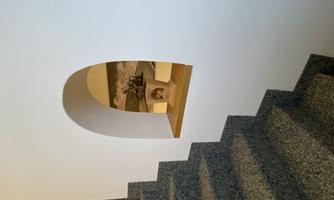 A staircase with gray steps leading to a white wall room. Behind a small window, a decorative element is visible.