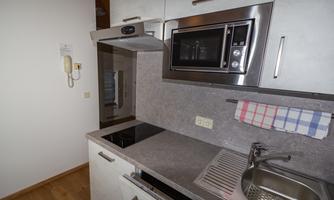 A modern kitchen with a stove, a microwave, and a sink. The walls are light, and there is a striped kitchen towel.