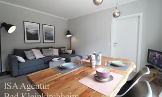 A modern living room with a gray sofa and a large dining table. Pictures hang on the walls and the lighting is stylish.
