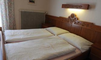 A cozy room with two beds and wooden furniture. The window is adorned with curtains and a picture hangs on the wall.