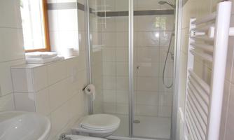A modern bathroom with a shower cubicle, a sink, and a toilet. The walls are light tiled and there is a window for natural light.