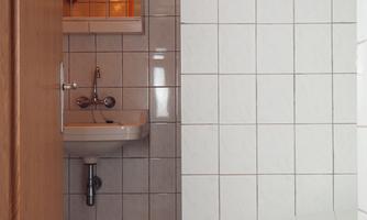A small bathroom with white tiles. Visible are a sink, a toilet, and a rug on the floor.