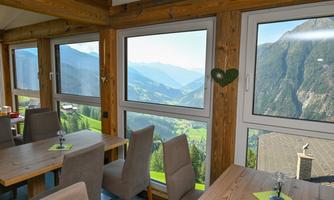 A cozy restaurant with wooden decor and a view of picturesque mountains. The large windows offer a stunning view of the surrounding landscape.