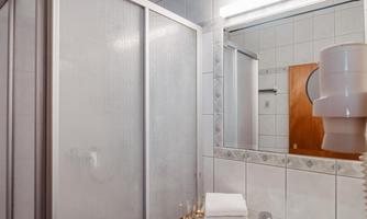 A modern bathroom with a shower cubicle and a sink. The walls are tiled and there is a mirror light.
