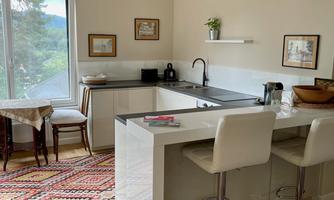 A modern kitchen with bar stools and an adjacent dining area. Plenty of daylight pours in through the window, creating a bright atmosphere.