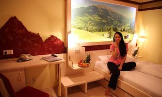 A cozy room with a single bed and a beautiful landscape wall. A woman is sitting on the bed and enjoying fresh fruit.