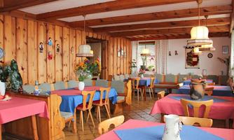 An inviting dining room with wooden walls and colorful tablecloths. There are cozy seating areas and decorative plants.