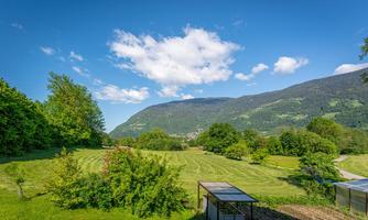A green landscape with gentle hills and trees. The sky is clear and blue with a few clouds.