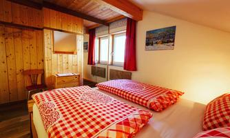 A cozy bedroom with two beds and red-and-white checkered bedding. The walls are made of wood and there are large windows that let in plenty of light.