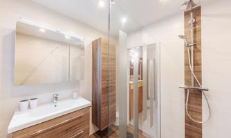 A modern bathroom with a glass shower and wooden shelves. The room is bright and cheerfully designed.