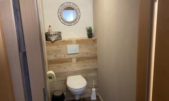 A modern bathroom with a toilet and wooden paneling. A round mirror is hanging on the wall and a small plant is standing on the shelf.