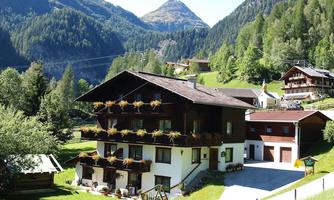 A pretty alpine building with flower balconies in a picturesque landscape. Surrounded by green forests and mountains.