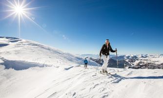 A sunny, snow-covered mountain with skiers. The sky is clear and blue, ideal for winter sports.