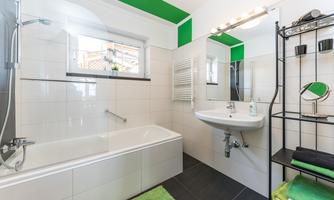 A modern bathroom with a bathtub and a shower. Bright tiles and green accents give the room a fresh atmosphere.