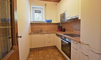 A modern kitchen with white cabinets and wood paneling. It features a sink, a stove, and a microwave oven.
