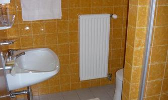 A small bathroom with orange tiles. There is a shower, a sink, and a toilet.