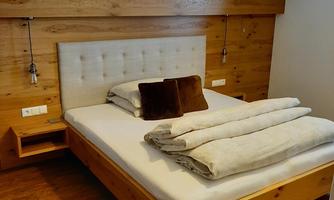 A cozy bedroom with a large wooden bed and a warm atmosphere. The wall is paneled with wood, and there is a pretty lampshade above the bed.