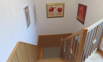 A bright staircase with a wooden railing leads down. Several pictures hang on the walls, decorating the space.