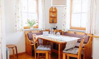 A cozy dining area with a wooden bench and a wooden table. Large windows let in plenty of light, and fresh flowers bring color to the room.
