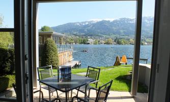 A beautiful view of the lake with mountains in the background. The outdoor area is equipped with a table and chairs, perfect for relaxing.