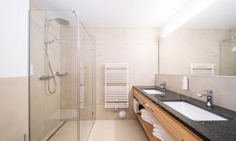 A modern bathroom with a shower and two sinks. The walls are brightly tiled and there is a wooden cabinet.