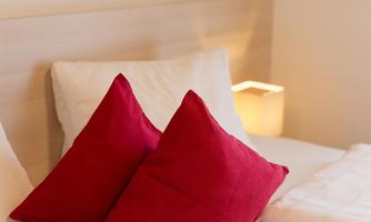 A cozy bed with red pillows and a warm lamp. The decor is modern and inviting.