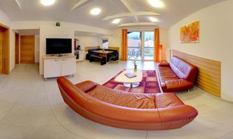 A modern living room with a red sofa and a television. Large windows provide plenty of light and a view outside.