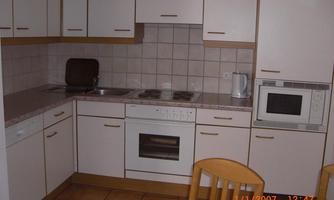 A modern kitchen with white cabinets and an oven. The room also contains a stove, a microwave, and a table with chairs.