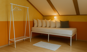 A cozy room with a bed system and colorful walls in yellow and orange. There is a white clothing rack and several cushions on the bed.