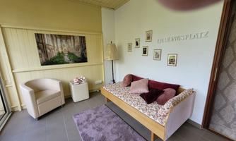 A cozy room with a comfortable sofa and a reading chair. Pictures hang on the wall, and a lamp provides pleasant light.