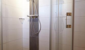 A modern shower with glass walls and an elegant showerhead. The floor is in a gray tone.