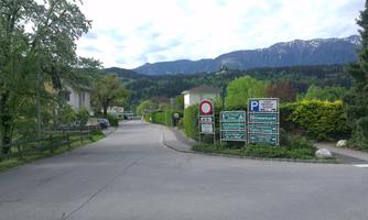 A quiet street with views of mountains and green surroundings. Various traffic signs and parking options are visible.