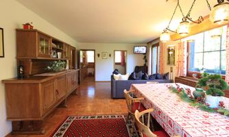 A cozy living area with a large dining table and a wooden dresser. The room is bright and cheerful, with windows that let in plenty of daylight.