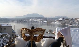 An elegant champagne cooler with bottles and a mask stands on a snow-covered terrace. In the background, a picturesque lake and snow-capped mountains can be seen.