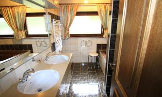 A modern bathroom with two sinks and a large mirror. The windows are decorated with colorful curtains.