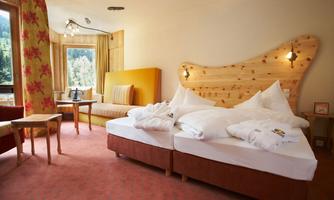 A cozy hotel room with two beds and warm wooden paneling. Large windows offer a view of nature, and the room is brightly and invitingly furnished.