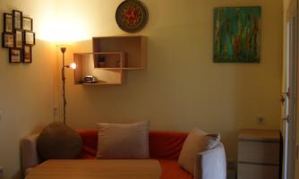 A cozy living room with a comfortable sofa and a table. The walls are decorated with pictures, and a lamp provides warm light.