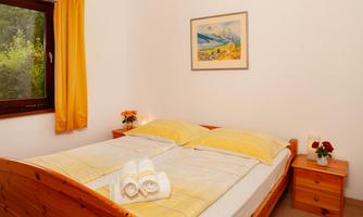 A cozy bedroom with a double bed and yellow bedding. The room has a window overlooking greenery and decorative flowers on the nightstand.