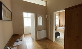 A bright hallway with wooden flooring and a wardrobe. In the background, there is an open entrance to a room.